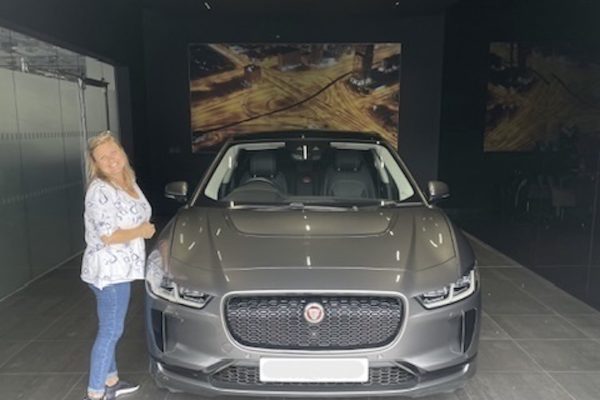 Michelle, smiling, standing next to her brand new car, a grey EV